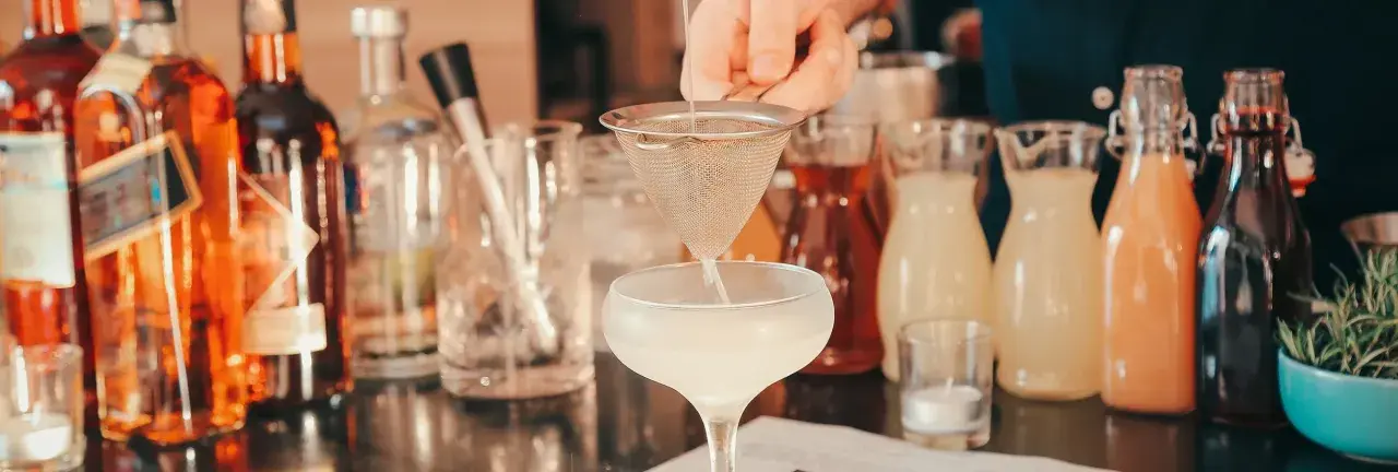 Ile napojów na wesele 80 osób? Barman przygotowuje drinka, w tle butelki z alkoholami i syropami.