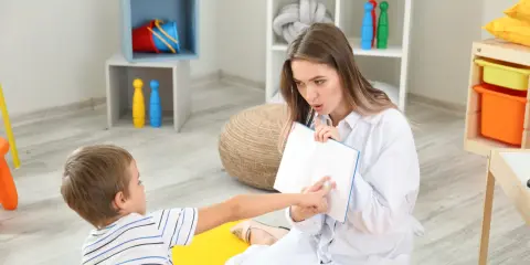 Terapeuta pracuje z dzieckiem nad poprawą niewyraźnej mowy, wskazując palcem na strony otwartej książki.