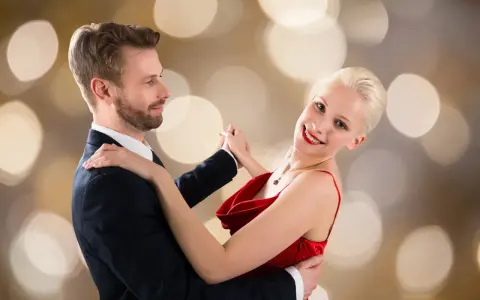 Para tańczy walca angielskiego na tle złotych bokeh. Ona w czerwonej sukni, on w garniturze.
