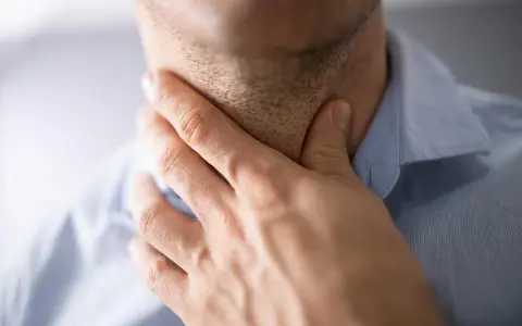 Mężczyzna trzyma się za gardło, szukając sposobów na zdarte gardło po koncercie.