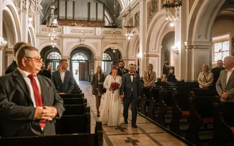 Para młoda idzie do ołtarza przy akompaniamencie piosenki na wejście. W kościele zgromadzeni goście.