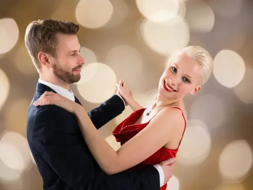 Para tańczy walca angielskiego na tle złotych bokeh. Ona w czerwonej sukni, on w garniturze.