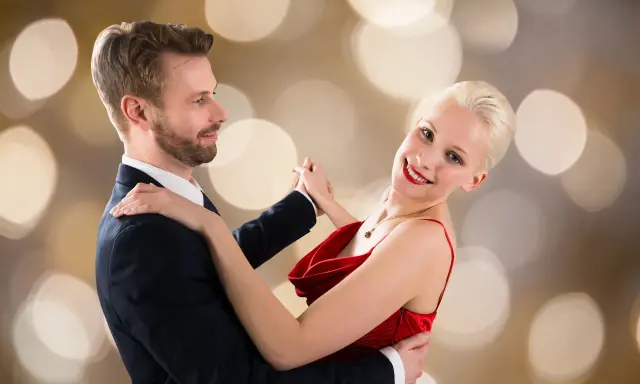 Para tańczy walca angielskiego na tle złotych bokeh. Ona w czerwonej sukni, on w garniturze.