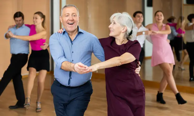 Uśmiechnięta para seniorów uczy się, jak tańczyć na 3, w tle inne pary.