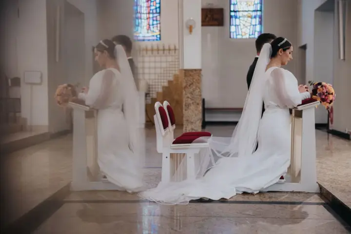 Para młoda klęczy przy ołtarzu. W tle witraże i ławki. Czyżby to były przesądy ślubne dla pana młodego?